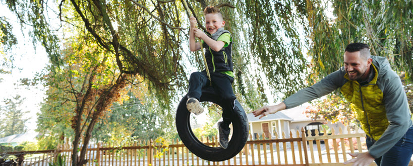 Father pushing his son on a tire swing in the backyard.