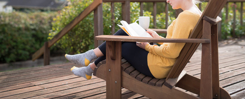 Femme lisant dans une chaise Muskoka sur une terrasse en bois.