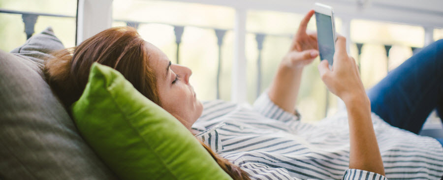 Une femme étendue sur un divan regarde son téléphone