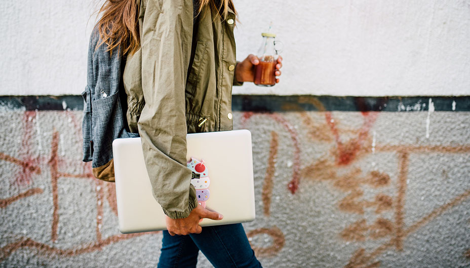 Teen walking with laptop in hand.