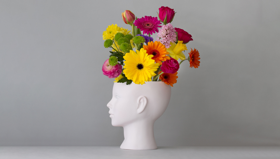 A vase in the shape of a human head holding a bouquet of flowers.