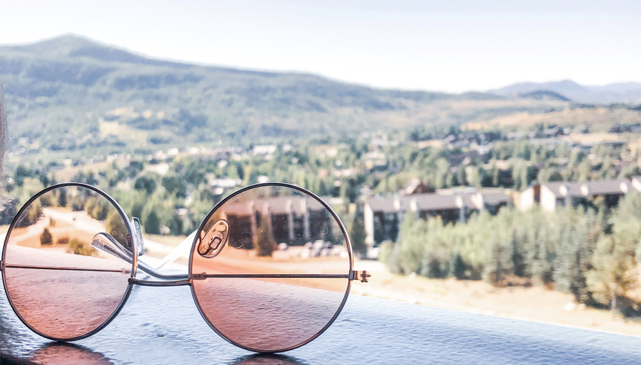 A pair of rose-coloured glasses sit on a porch railing.