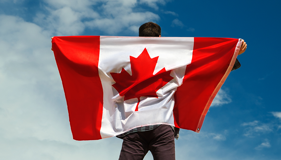 A man stands with a Canadian flag draped across his back.