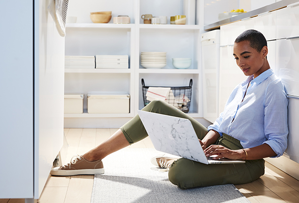Woman sitting on the kitchen floor with a laptop in her lap. 