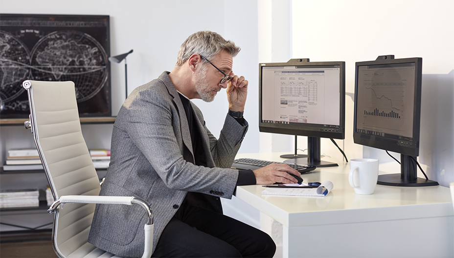 Un homme assis à un bureau regarde deux écrans d'ordinateur.