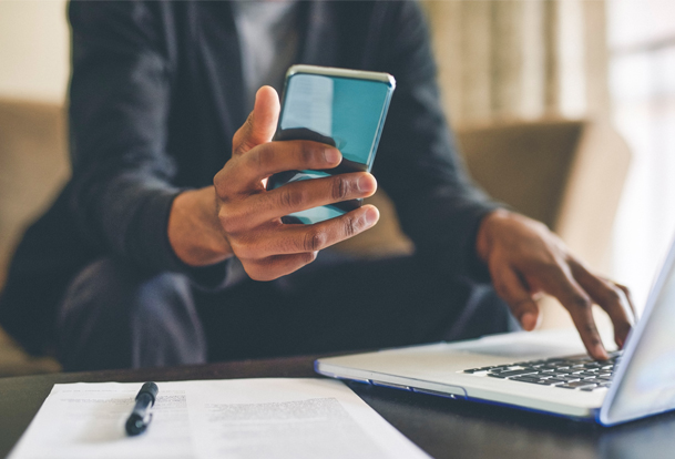 A close-up photo of someone working on a laptop with a cellphone in their other hand.