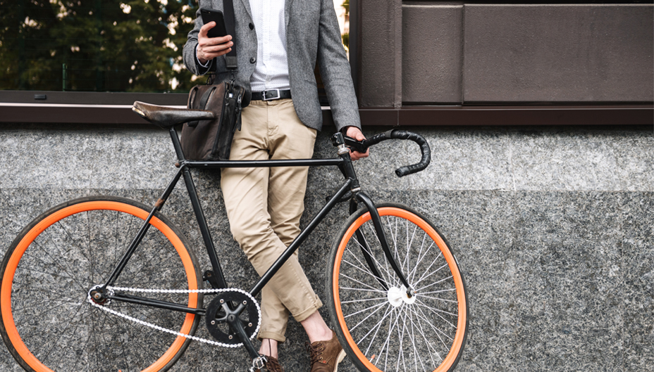 A man standing next to his bicycle while looking at a phone.