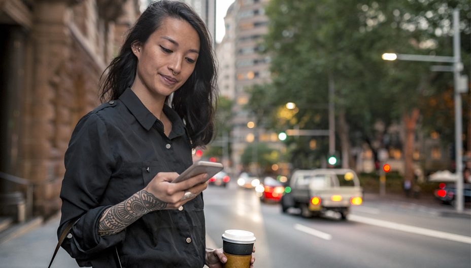A woman in the city holding a coffee and browsing her phone.