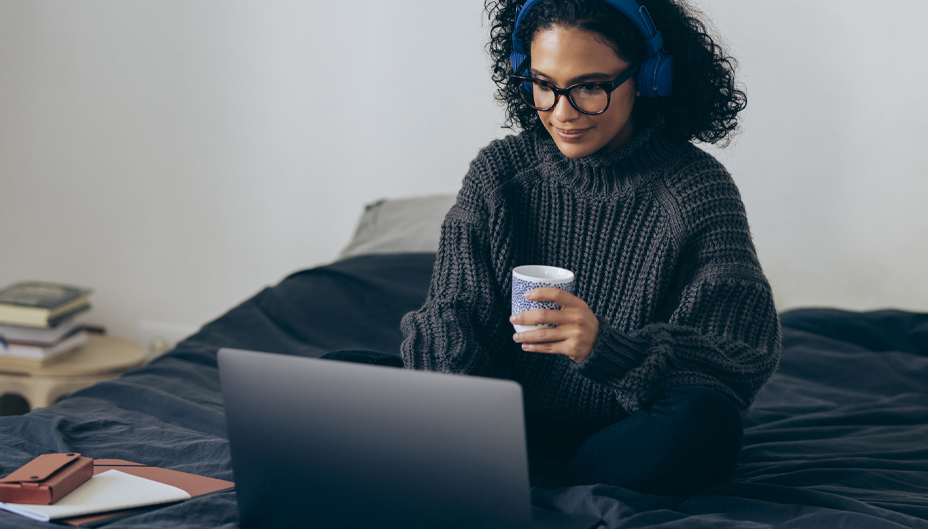 A woman with a coffee and headphones working on her laptop.