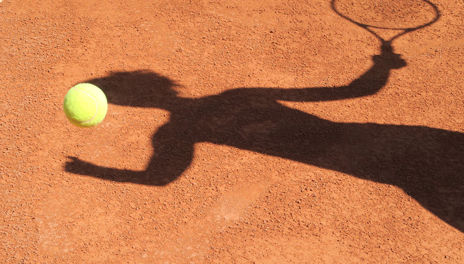 Shadow of a tennis player hitting the ball with their racket.