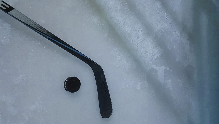 A hockey stick and puck lie on ice.