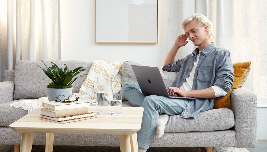 Un jeune investisseur assis sur un canapé utilise un ordinateur portable.