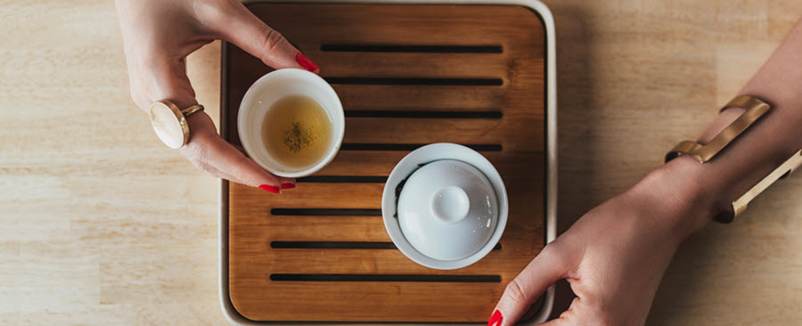 Bird's eye view of a woman's hands holding a cup of tea from a Chinese tea set.